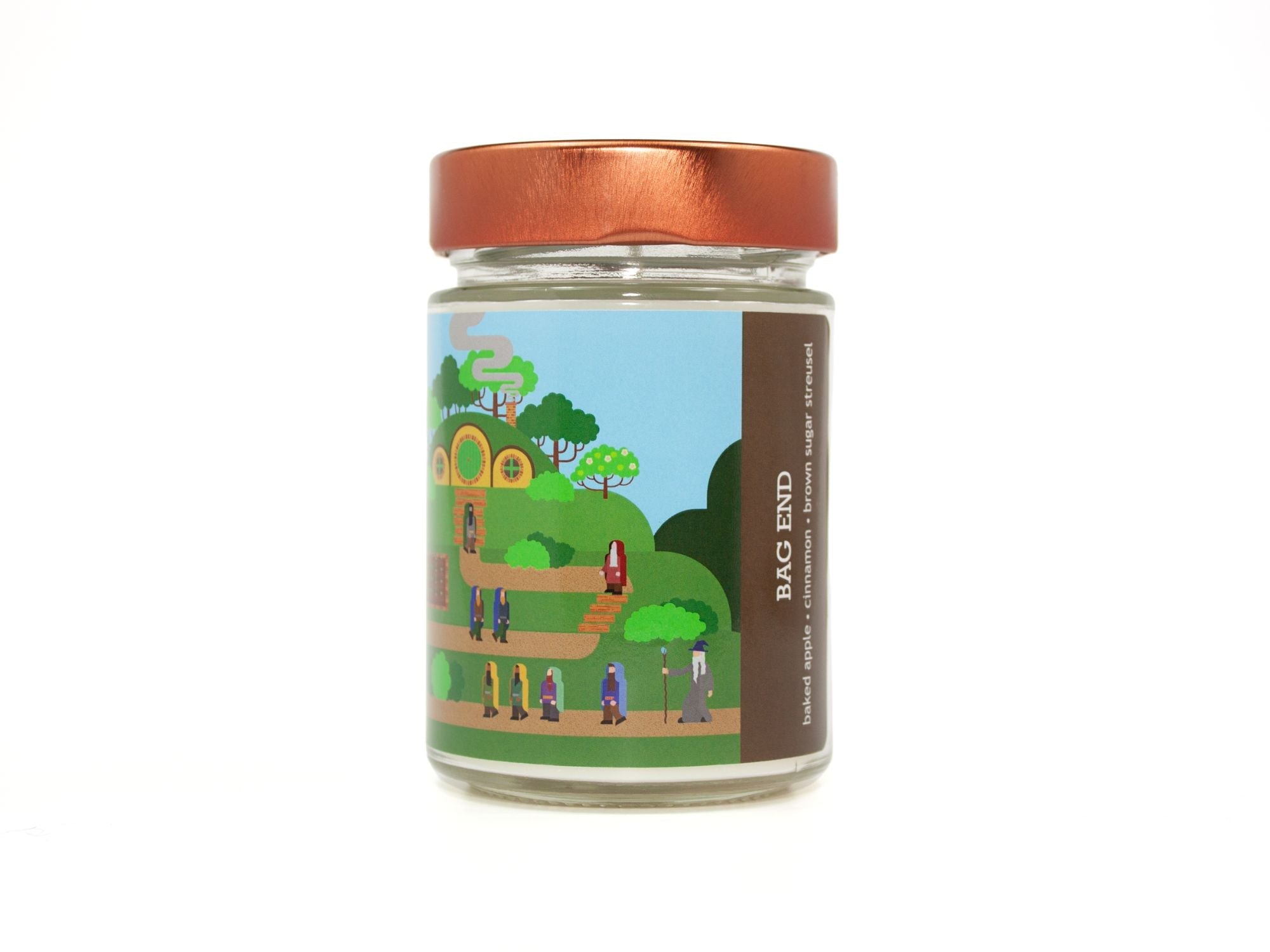 Onset & Rime apple tart scented candle called "Bag End" in a 10 oz glass jar with copper lid. The label depicts a scene from "The Hobbit" with dwarves and a wizard approaching Bilbo's cottage. The text on the label is "Bag End - Baked Apple, Cinnamon, Brown Sugar Streusel".