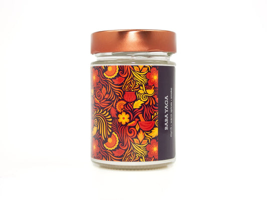 Onset & Rime spiced smoke scented candle called "Baba Yaga" in a 10 oz glass jar with copper lid. The label is purple-black with a bright red pattern of flames, swirls and flowers. The text on the label is "Baba Yaga - Myrrh, Warm Spices, Smoke".