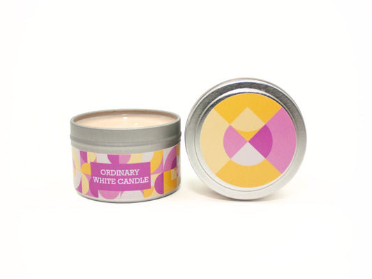 Onset & Rime flannel scented candle called "Ordinary White Candle" in a 4 oz silver tin. The circular label on top is a geometric pattern of pink, yellow and white circles and teardrops. The text on the front label is "Ordinary White Candle - Warm Flannel, Lemon Blossom, Sheer Musk".