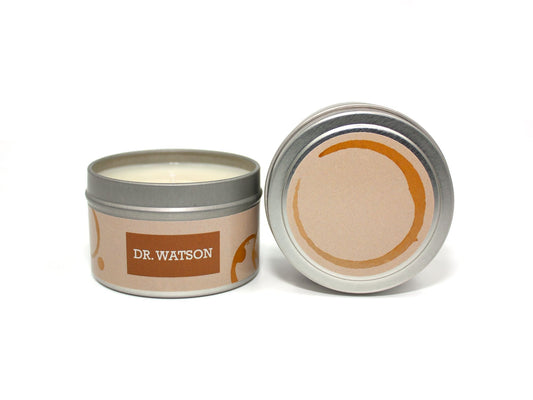Onset & Rime tea and old books scented candle called "Dr. Watson" in a 4 oz silver tin. The circular label on top is the colour of aged paper with a circular tea stain. The text on the front label is "Dr. Watson - Black Tea, Old Books".
