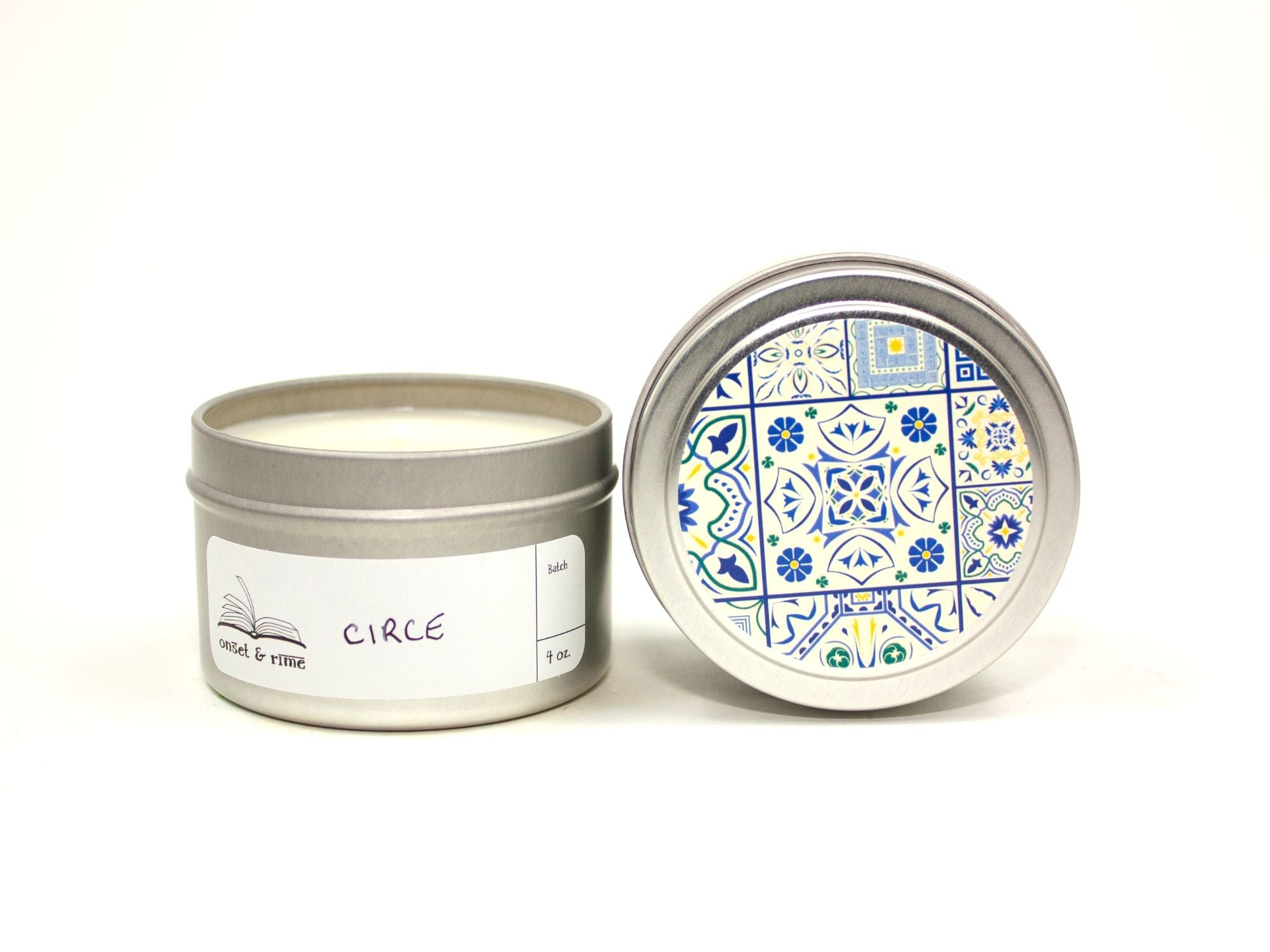 Onset & Rime lemon, cypress scented candle called "Circe" in a 4 oz silver tin. The circular label on top is white with a dark blue Greek tile pattern. The scent name is handwritten on a white rectangular label on the side of the tin.